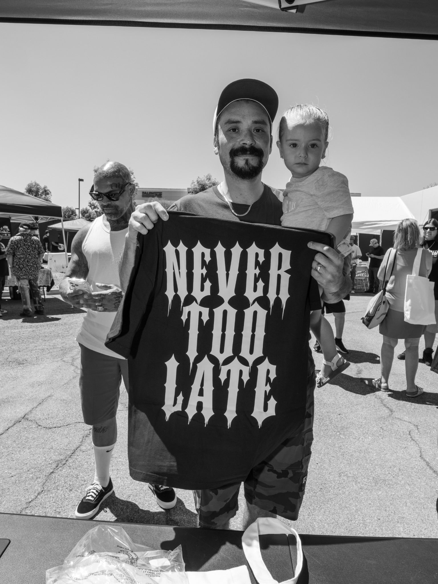 A member of the community holding a child and a Never Too Late shirt